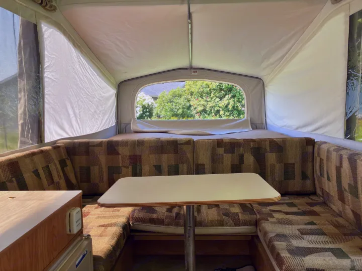Interior of a pop-up camper rv rental, showing a comfortable dinette with patterned cushions and a bright window view.. Jayco Qwest 2003