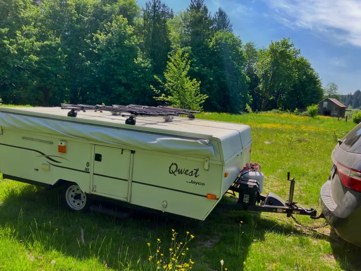 Jayco Qwest pop-up camper with Thule racks, hitched to a car in a sunny field. Ideal for an RV rental camping trip.. Jayco Qwest 2003