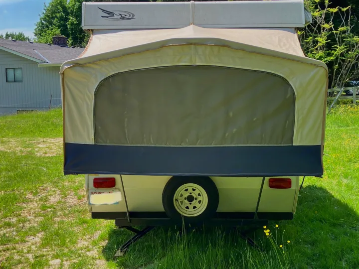 This pop-up camper, seen from the rear with its tan fabric top & screen, is perfect as an rv rental. Spare tire shown.. Jayco Qwest 2003