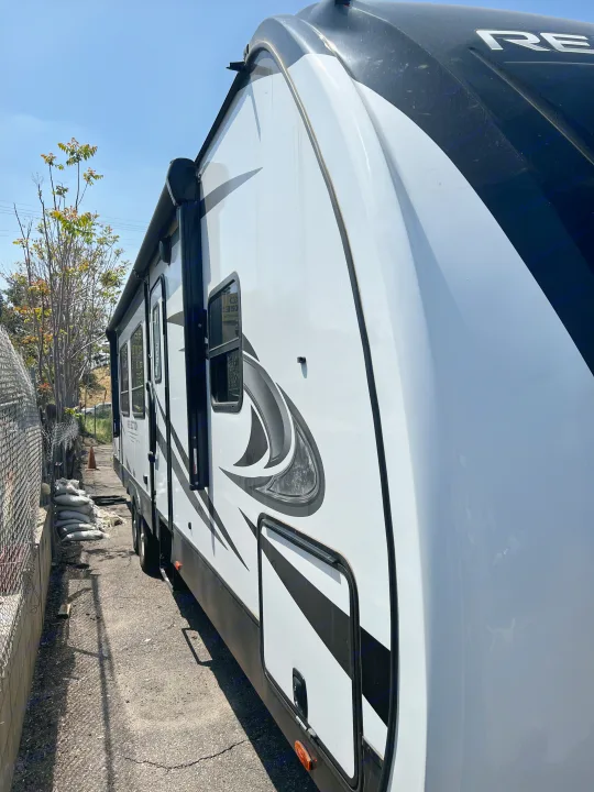 Large white and black travel trailer, an RV rental, parked on asphalt in a sunny outdoor setting.. Grand Design Reflection 2022