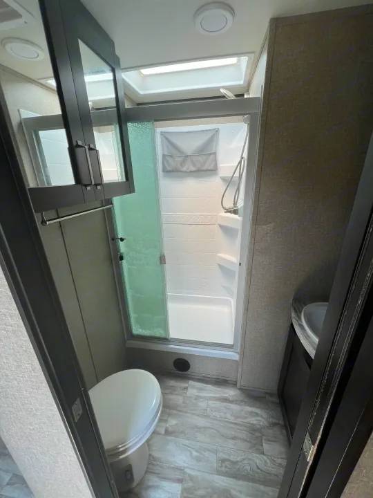 This RV rental's compact bathroom features a toilet, glass shower, sink, and mirror—perfect for travel adventures.. Grand Design Reflection 2022