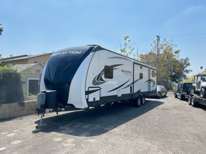 A sleek white & black Grand Design Reflection travel trailer, parked on asphalt under a clear sky, ready for rv rental.. Grand Design Reflection 2022