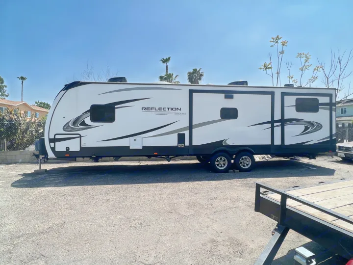 A large white Grand Design Reflection travel trailer, excellent for RV rental, parked outdoors on a sunny day.. Grand Design Reflection 2022