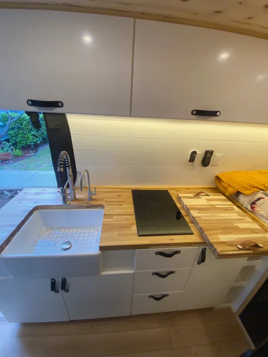Modern **RV rental** kitchen: white cabinets, butcher block counters, farmhouse sink, and induction. Mercedes-Benz Sprinter 2022