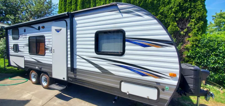 This sleek white travel trailer RV, perfect for rv rental, features blue and orange decals, an awning, and multiple windows.. Forest River Salem Cruise Lite 2018