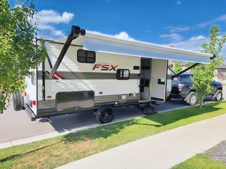Wildwood FSX travel trailer with an extended awning and open door, parked on a sunny day; ideal for RV rental adventures.. Forest River Wildwood FSX 2021