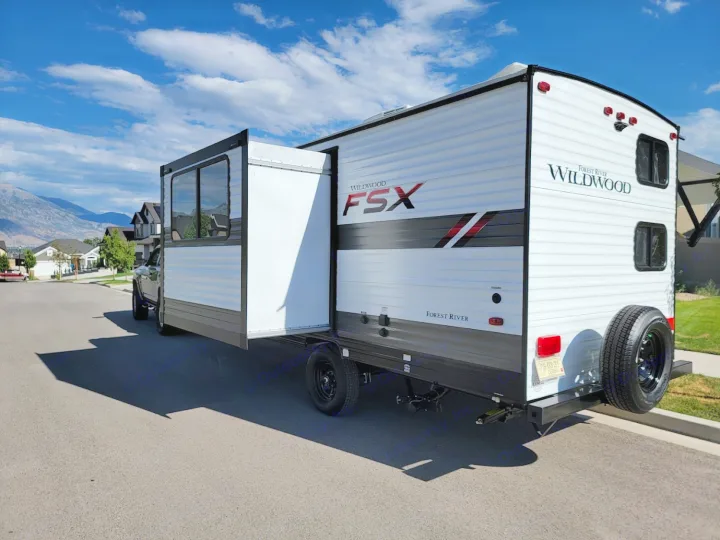 White Forest River Wildwood FSX travel trailer with extended slide-out, ready for an RV rental adventure, parked on a sunny street.. Forest River Wildwood FSX 2021