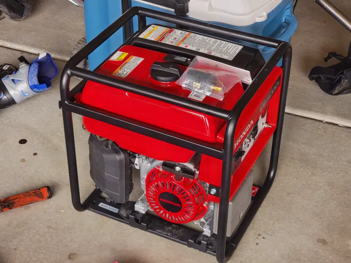 A red Honda portable generator, likely for RV rental use, sits on a concrete floor, providing reliable power within its protective frame.. Forest River Wildwood FSX 2021