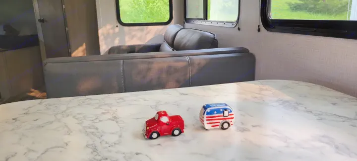 Bright RV rental interior with marble table, charming truck and camper shakers. Green nature visible outside.. Dutchmen Coleman Light 2022
