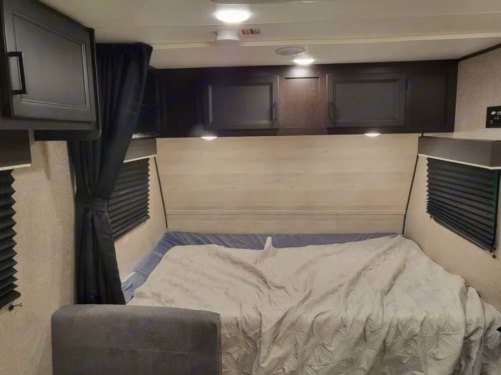 Explore this RV rental's cozy bedroom. It features a bed, overhead cabinets, and pleated window blinds.. Jayco Jay Flight SLX 2022