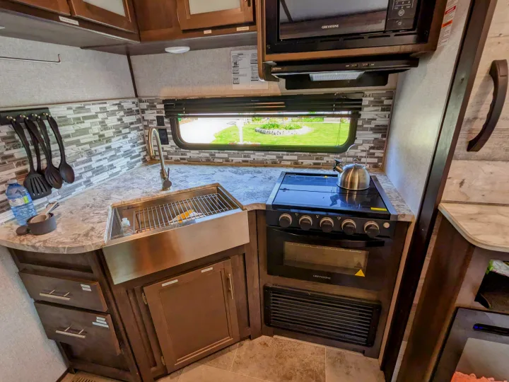 Modern RV rental kitchen with stainless sink, stove, microwave, and ample storage. Perfect for cooking while camping.. Coleman Lantern 2021