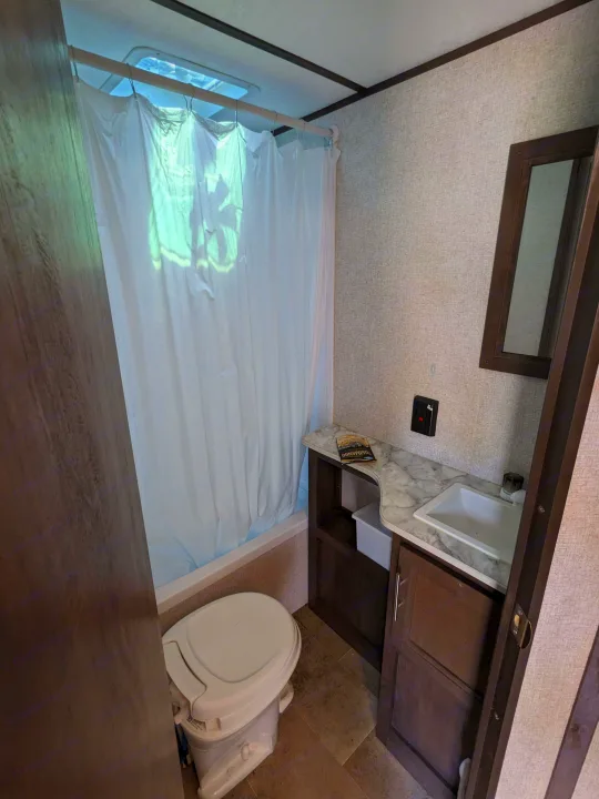 Functional RV rental bathroom with white shower curtain, toilet, vanity with sink, and skylight above the shower.. Coleman Lantern 2021