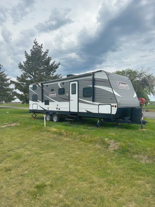 A Coleman travel trailer (RV rental) is parked on a grassy site under a cloudy sky, ready for a camping trip.. Dutchmen Coleman Lantern 2019