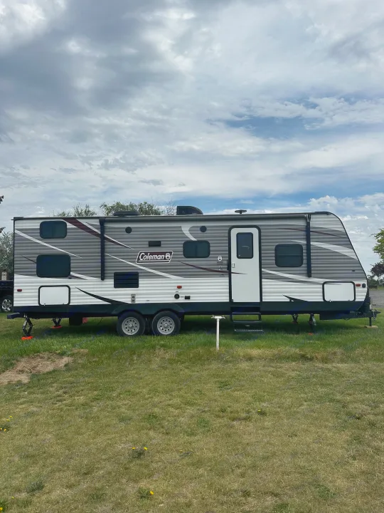 A grey Coleman RV rental is parked on green grass under a cloudy sky.. Dutchmen Coleman Lantern 2019