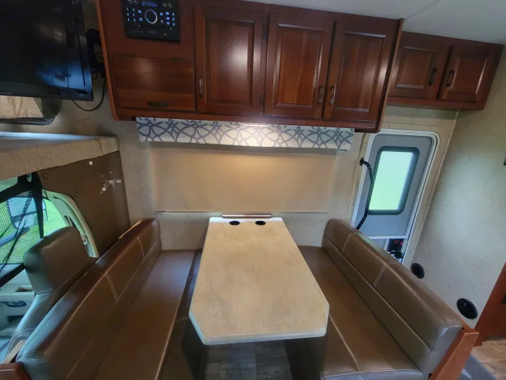 Inside an RV rental: a brown dinette with a light table, dark wood cabinets, TV, and window shade. Ready for adventures.. Forest River Sunseeker 2017