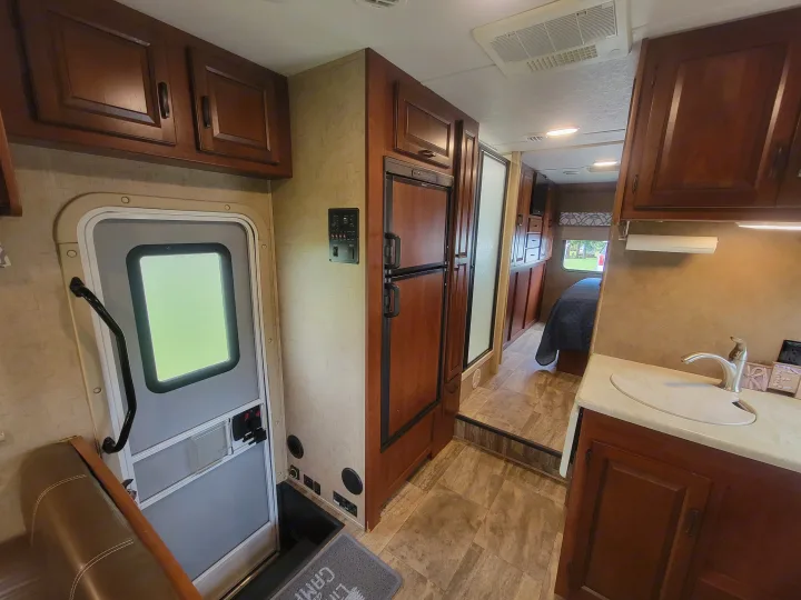 View inside an **rv rental** showing the compact kitchen with sink and fridge, leading back to a bedroom with a visible bed.. Forest River Sunseeker 2017
