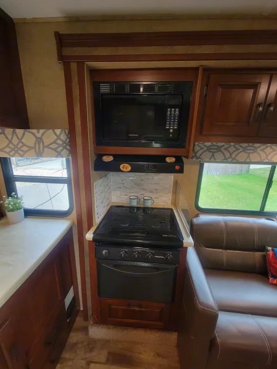 Cozy RV rental kitchen with a microwave, stove, cabinets, mosaic backsplash, and brown sofa, ready for your adventure.. Forest River Sunseeker 2017
