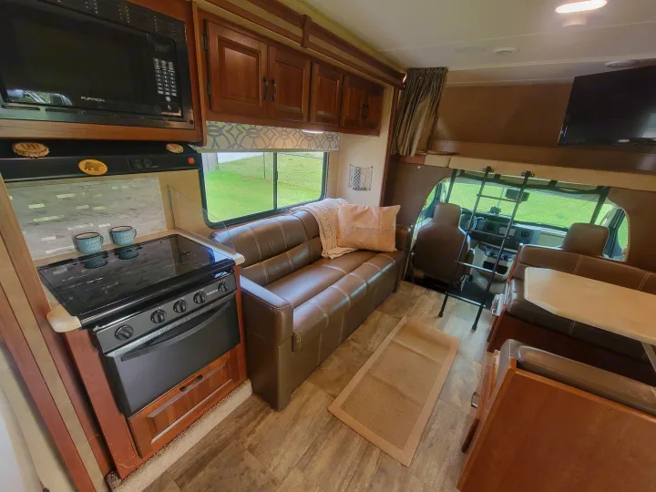 RV rental interior: fully equipped kitchen (microwave, stove), comfy sofa, dining area, and front bunk. Ready for your trip!. Forest River Sunseeker 2017
