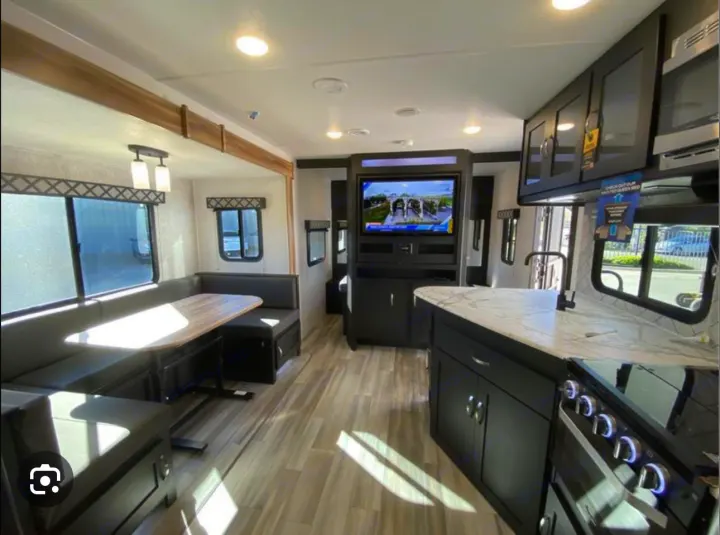 Modern RV rental interior with kitchen, dining booth, and living space featuring a TV.. Coachmen 257BHS 2022