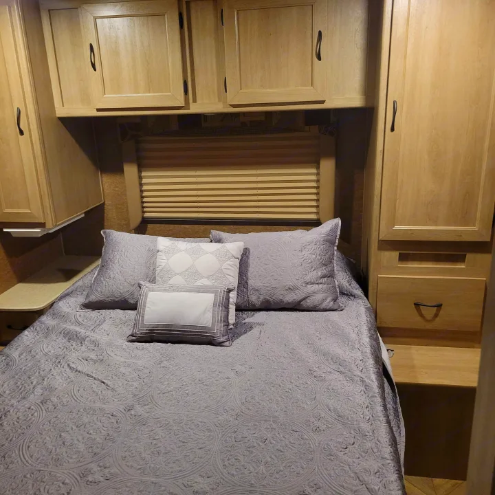 Cozy RV bedroom with gray bedding, built-in storage, and window blinds, perfect for an RV rental.. Forest River Coachmen Freelander 2016