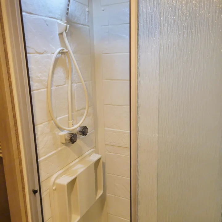 The functional shower space in an RV rental, complete with handheld sprayer, temperature controls, and shelf.. Forest River Coachmen Freelander 2016