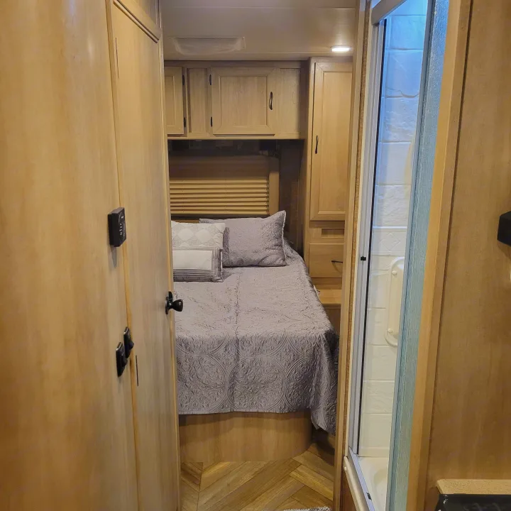 Inside an **rv rental**: a cozy bedroom with wood cabinetry and a shower on the right. Perfect for travel.. Forest River Coachmen Freelander 2016