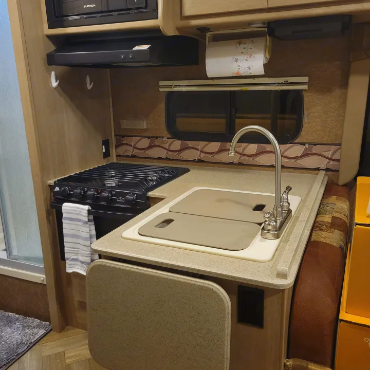 Compact rv rental kitchen with stove, sink, microwave, and shower visible, ideal for travel adventures.. Forest River Coachmen Freelander 2016