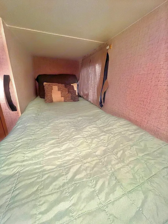 This RV rental features a compact, cozy sleeping bunk with a light green quilted bedspread and decorative pillow.. Winnebago Micro Minnie 2100BH 2022