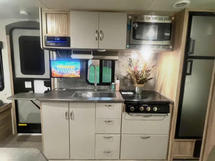 This compact, modern RV rental kitchen features a sink, stove, microwave, and refrigerator, ideal for travel adventures.. Winnebago Micro Minnie 2100BH 2022