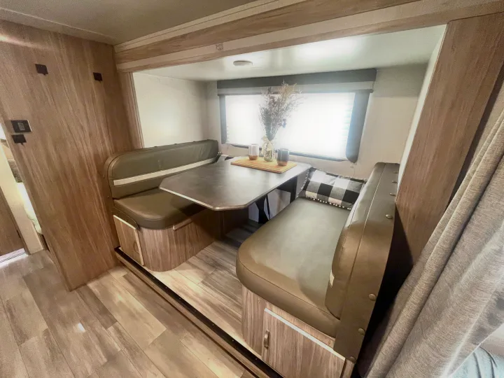 Cozy RV rental dinette interior: light wood, dark upholstered benches, a table, and a bright window with decor.. Winnebago Micro Minnie 2100BH 2022
