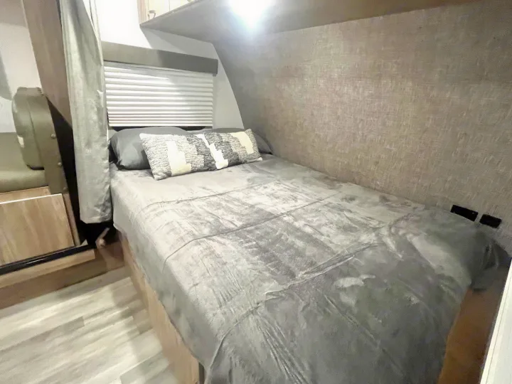Cozy RV rental bedroom features a bed with gray bedding, a patterned pillow, and window blinds.. Winnebago Micro Minnie 2100BH 2022