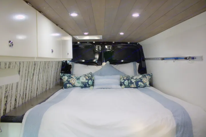 Cozy RV rental bedroom with a comfy bed, white bedding, floral pillows, wood ceiling, and birch tree wall decor.. Mercedes Sprinter 2012