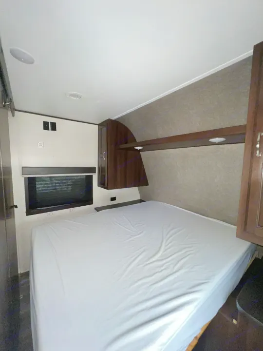 RV rental: Cozy bedroom showing a bed with white sheet, emergency exit window, and wood cabinetry.. Jayco Jay Flight 2018