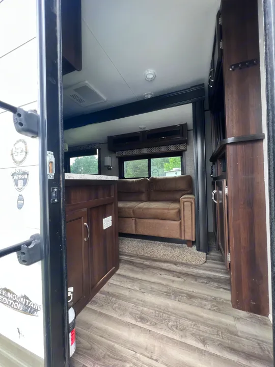 Inside an RV rental: view from the entry showing a brown sofa, kitchen counter, and overhead cabinets in the cozy living space.. Jayco Jay Flight 2018