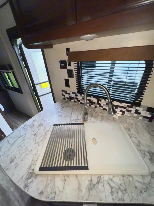 This RV rental kitchen features a marbled countertop, a modern sink with a drying rack, and a mosaic tile backsplash.. Jayco Jay Flight 2018