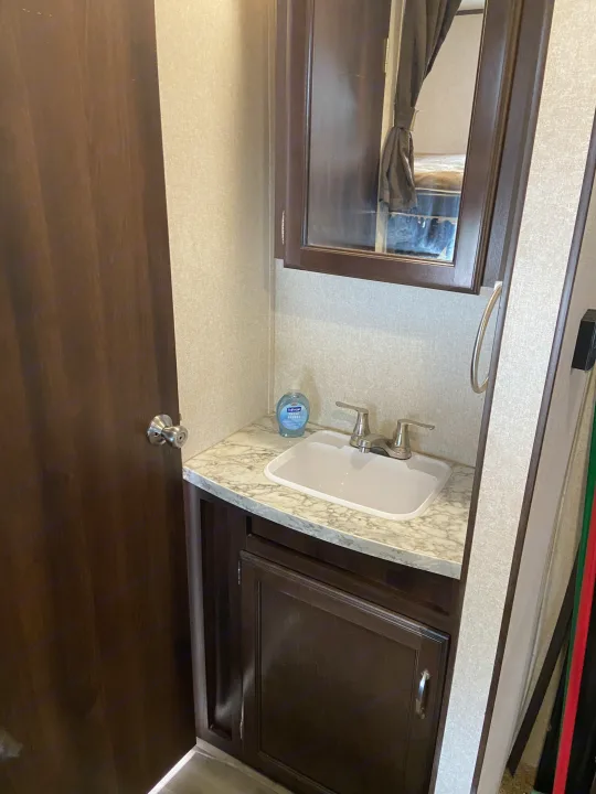 RV rental interior shows a compact bathroom with a sink, faucet, mirrored cabinet, and wood door.. Jayco Jay Flight SLX 2018