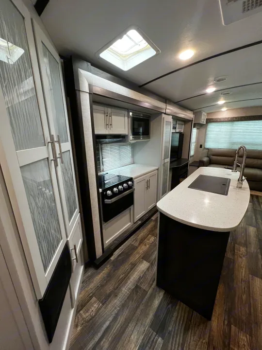 Spacious RV rental interior featuring a modern kitchen with island and stove, alongside a comfortable living area.. Keystone RV Bullet Premier Ultra 2020