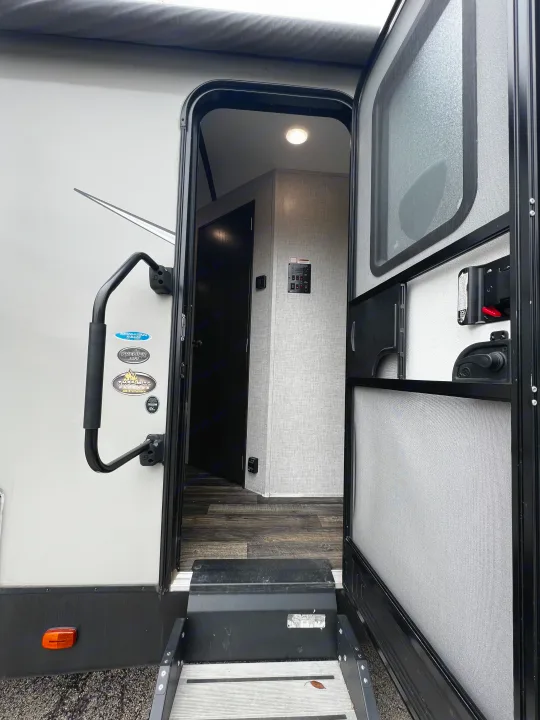 Open door of an RV rental, revealing interior steps and control panel. A grab handle is on the exterior.. Keystone RV Bullet Premier Ultra 2020