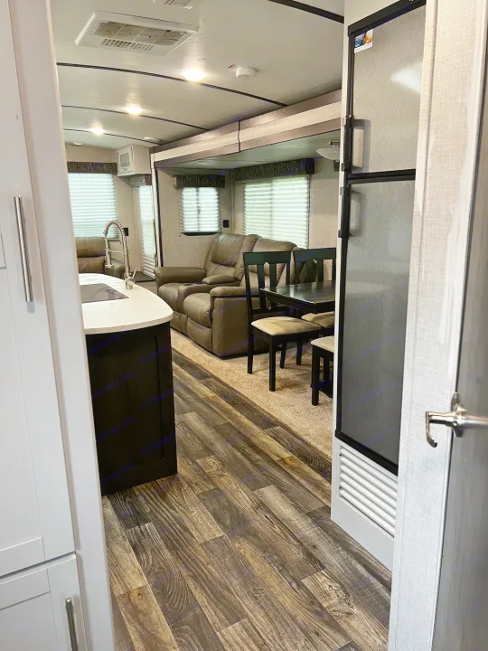 RV rental interior showing a spacious living area with recliners, dining table, and kitchen island. Dark wood flooring.. Keystone RV Bullet Premier Ultra 2020
