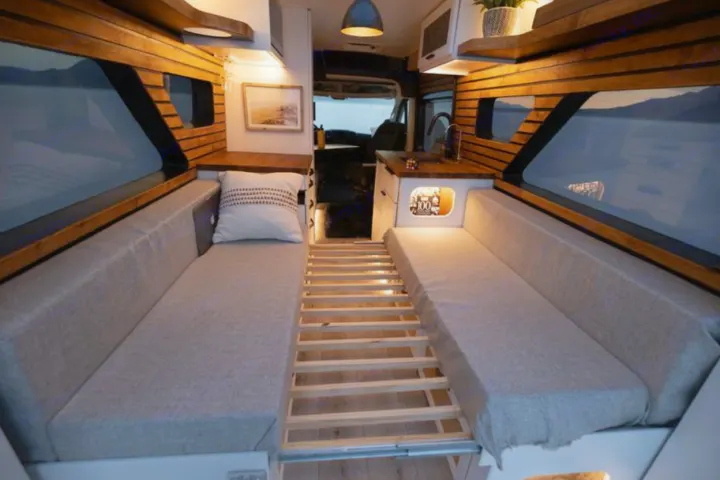 Modern rv rental camper van interior. Comfy bench seats, pull-out bed frame, wood paneling, and large windows for travel.. Dodge B Van 2020