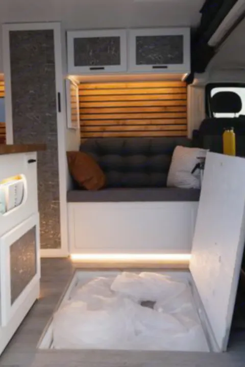 Step inside this RV rental's inviting interior with a cozy bench, wooden accent wall, and unique floor storage.. Dodge B Van 2020