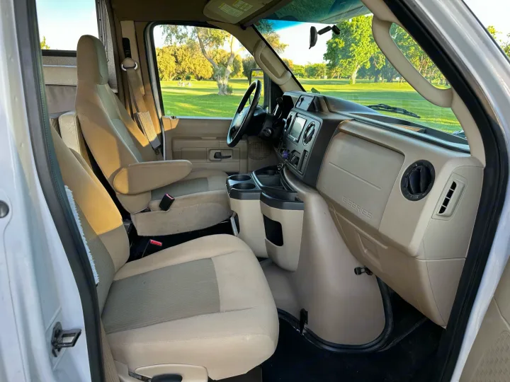 Spacious tan interior of an RV rental, showing front and passenger seats, dashboard, and outdoor view.. Winnebago Outlook 2019