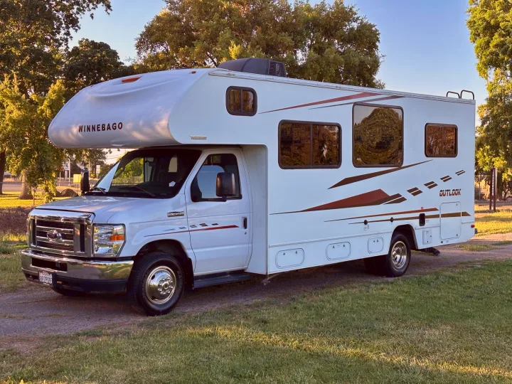 White Winnebago Outlook rv rental parked on a path near grass, ready for travel adventures.. Winnebago Outlook 2019