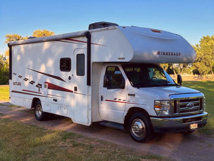 A bright white Class C Winnebago Outlook RV rental is parked on a dirt path under a clear blue sky.. Winnebago Outlook 2019