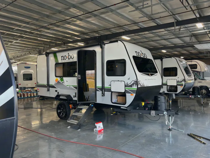 A sleek white 'no bo' travel trailer is showcased indoors. Explore this RV rental option for your next adventure!. No Boundaries 16 2023