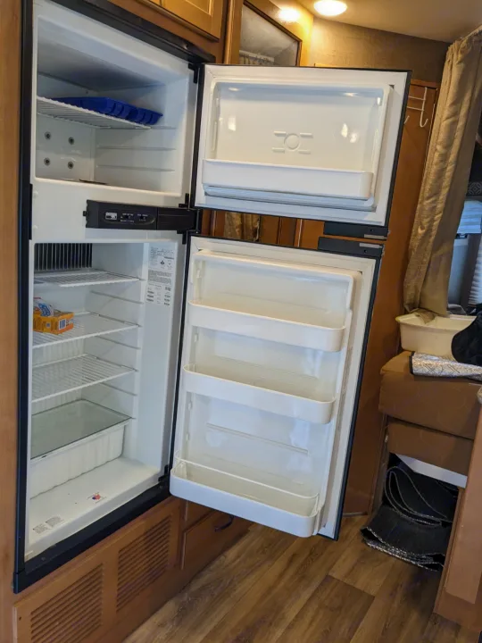 An open, mostly empty two-door refrigerator inside an RV rental, showing freezer and fridge compartments with shelves.. Thor Freedom Elite 2017