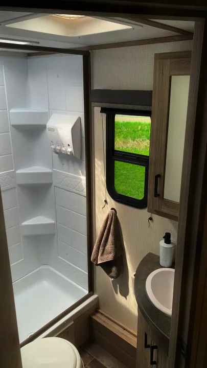 Explore a modern rv rental bathroom. It features a bright shower, a functional sink vanity, and a window with a green view.. Keystone RV Passport SL 2022