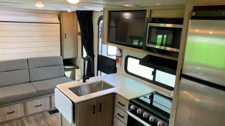 Inside a modern RV rental: a flexible living space with convertible sofa/bed, compact kitchen (sink, stove, microwave, fridge), and TV.. Keystone RV Passport SL 2022