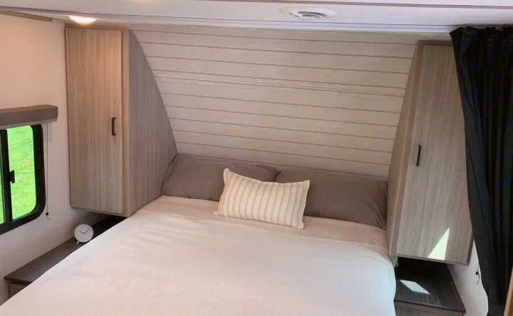 RV rental bedroom showcasing a neat bed, light wood-grain storage cabinets, and a shiplap-style accent wall.. Keystone RV Passport SL 2022