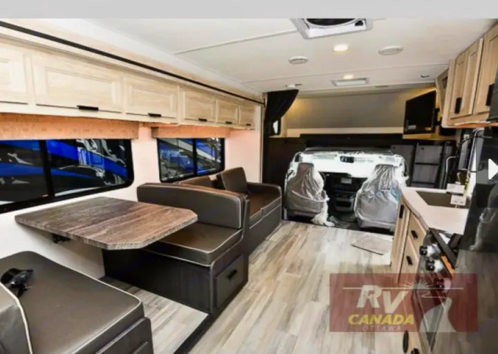 Inside a modern **rv rental**: a light-toned living space with a dining booth, sofa, and kitchen counter near the cockpit.. Forest River Sunseeker LE 2023